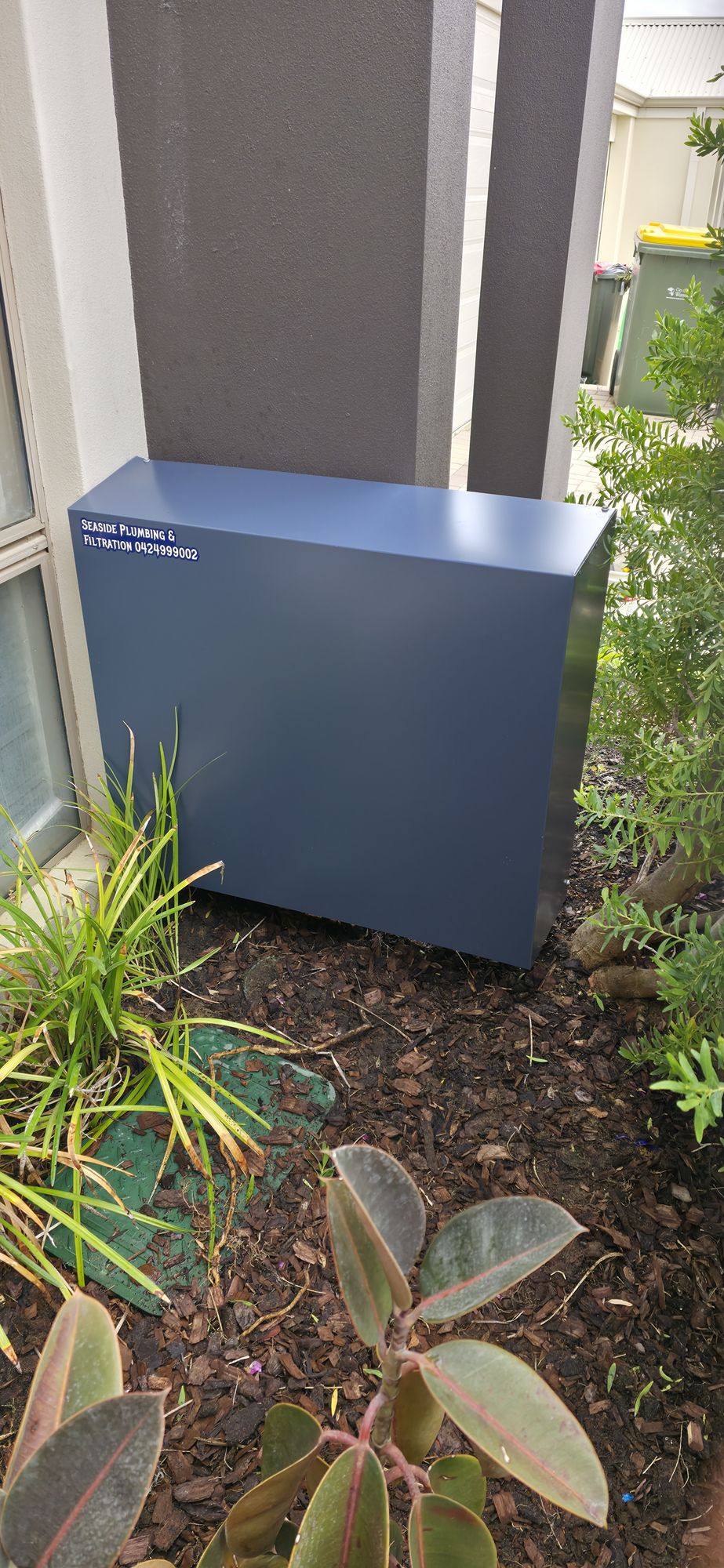 A blue-grey filter cover against a rendered wall among garden plants