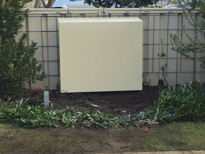 A cream filter cover on a side wall beside a fence, with new paving in front