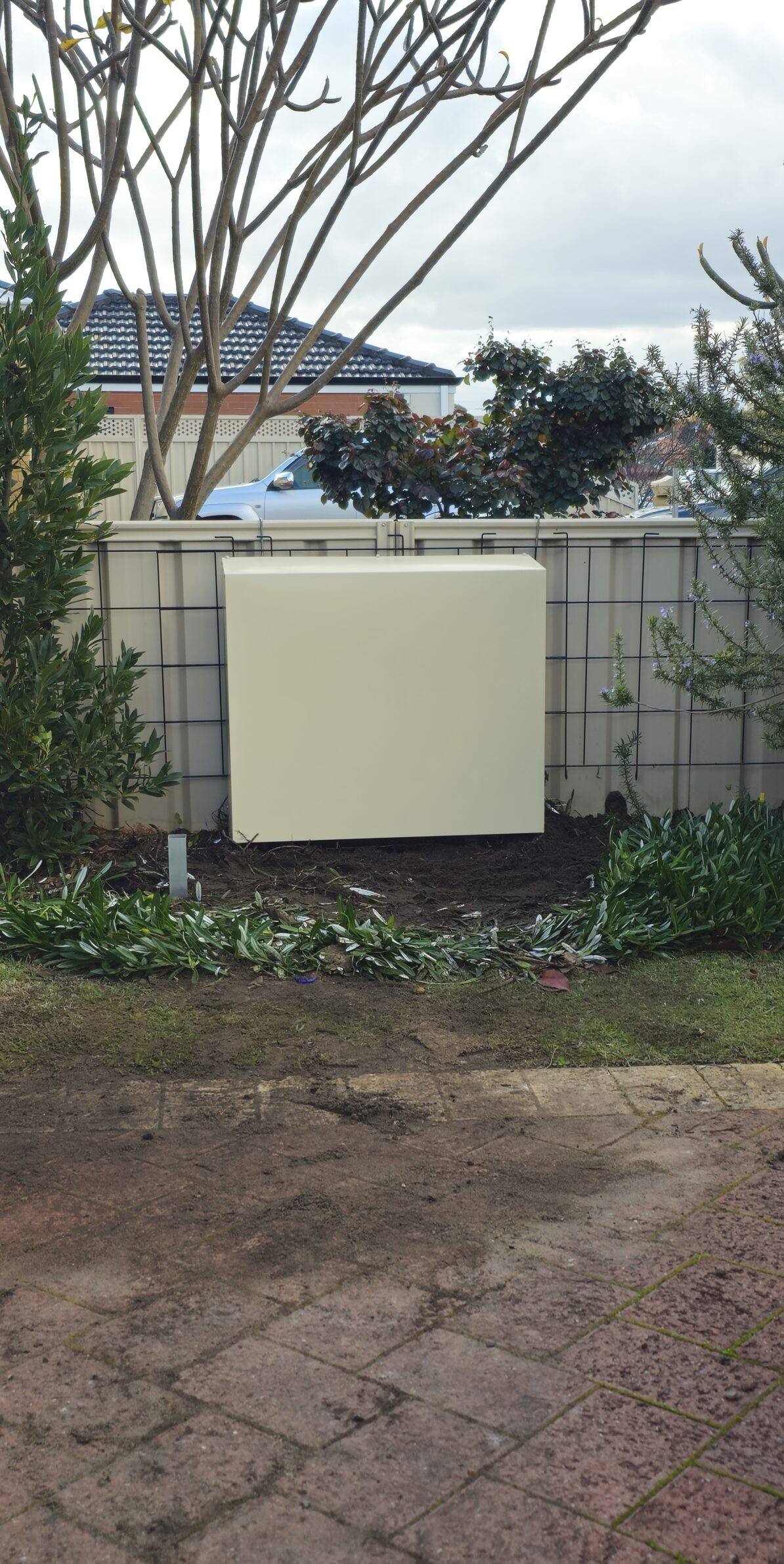 A cream filter cover on a side wall beside a fence, with new paving in front