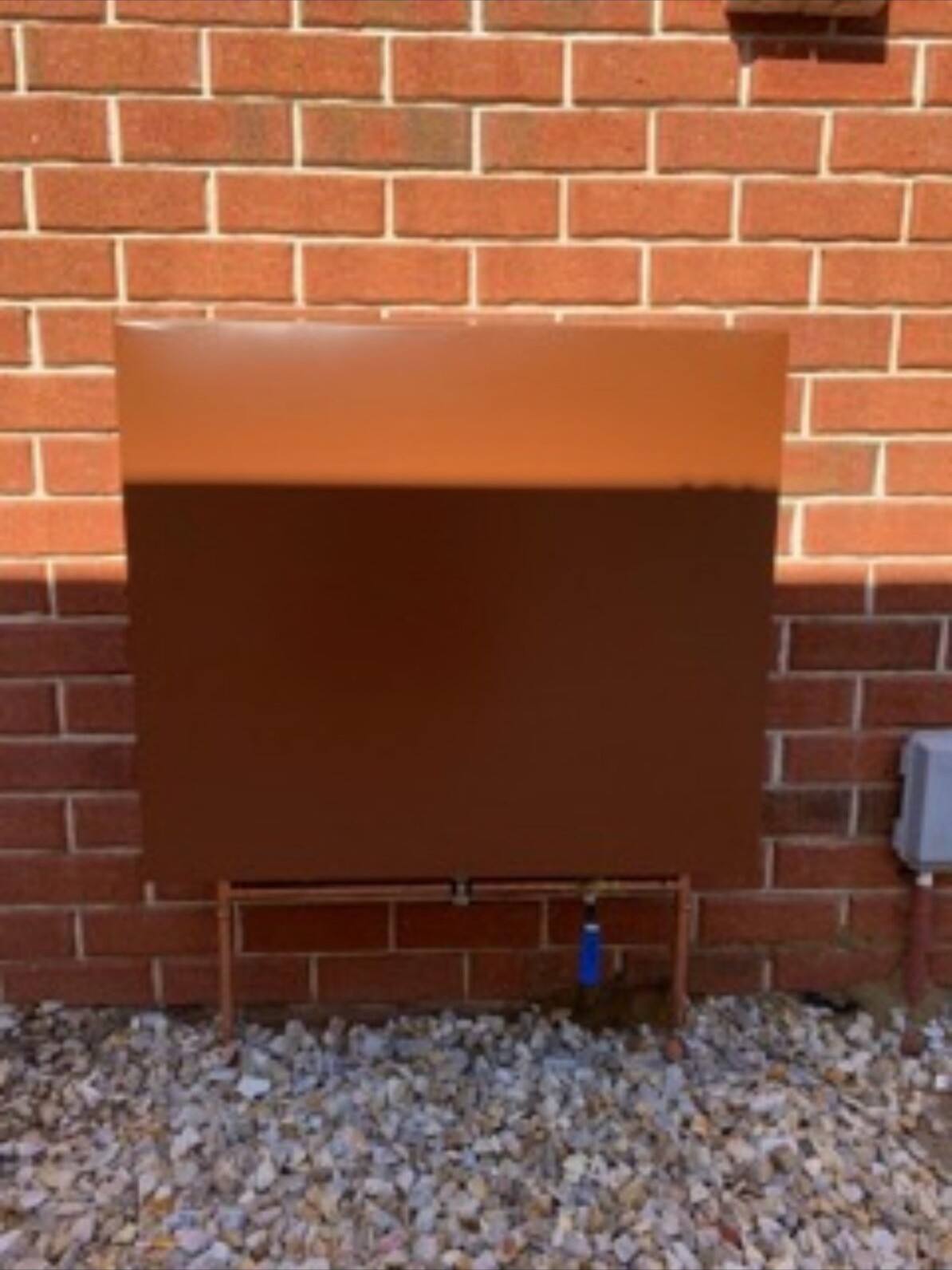 A filter cover painted terracotta to match the red brick wall behind it