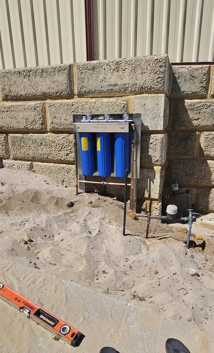 A whole-house filter being installed on a limestone wall, with a spirit level on the sand