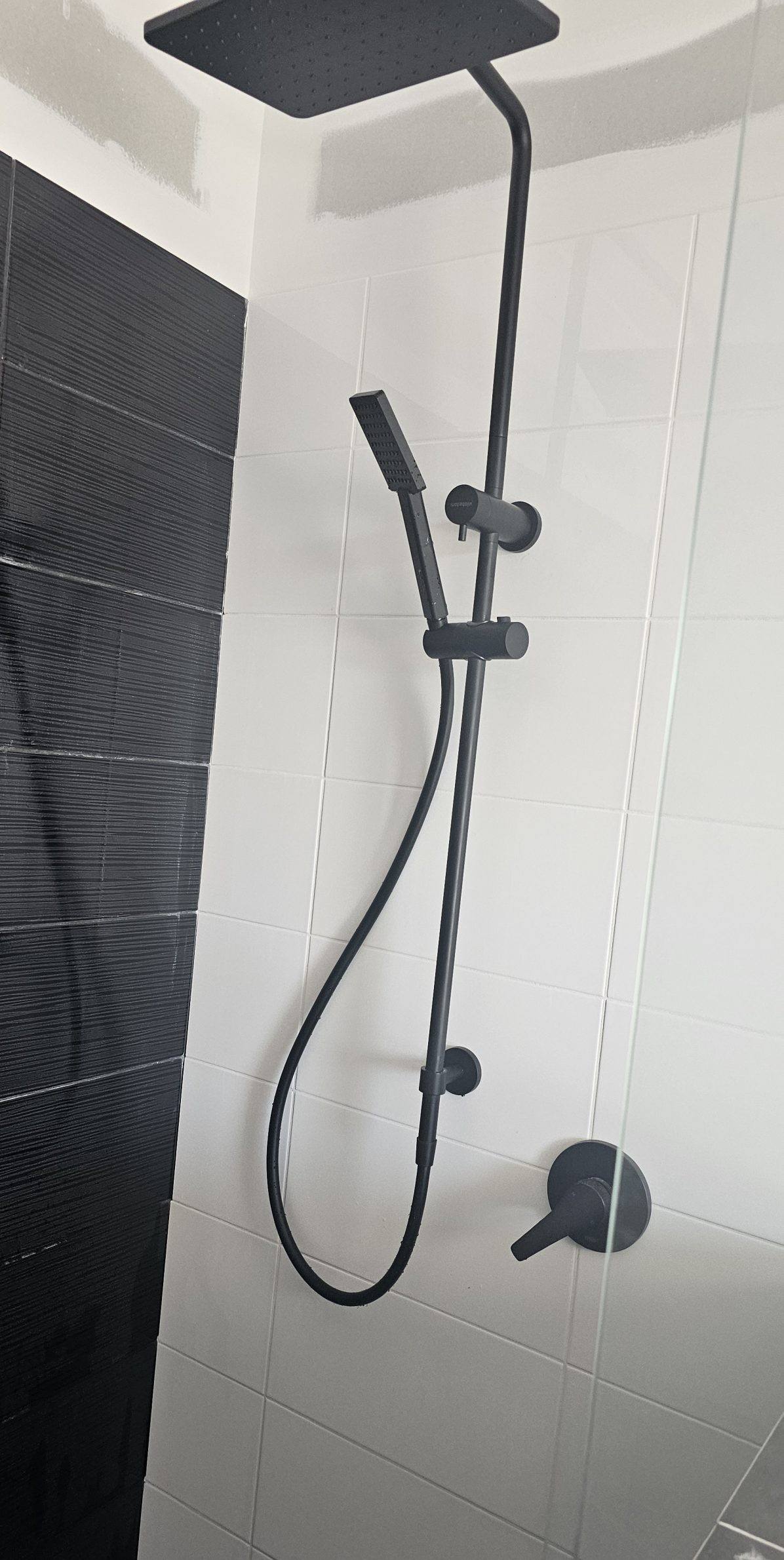 A matte black shower rail and mixer installed on white tiles