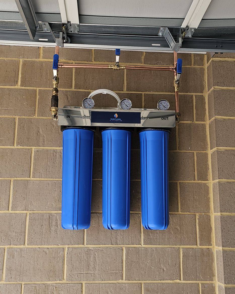 Three blue filter housings mounted on a brick wall beneath a raised garage door
