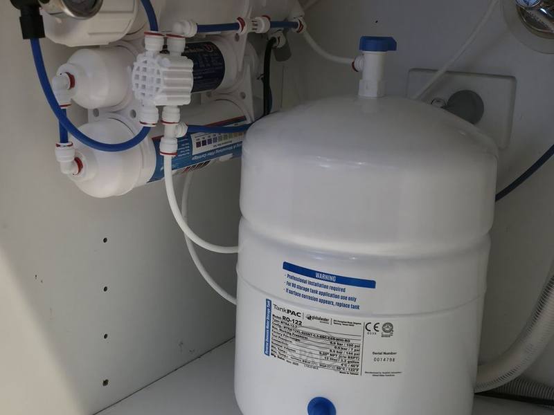 A reverse osmosis filter assembly and white storage tank in the cupboard beneath a kitchen sink